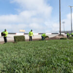A group of men in yellow jackets working on grass.