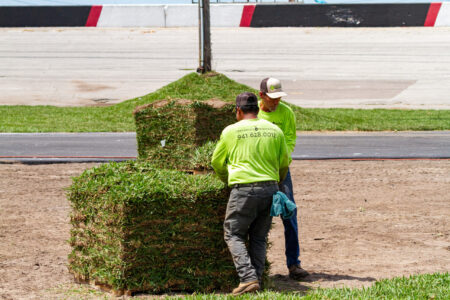 Two men in green shirts are working on a pile of grass.